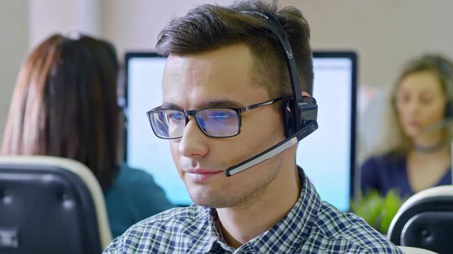 PAN of serious male call centre operator in glasses wearing headset with microphone and talking with client using voice call on computer 