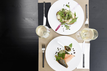 Meals for two at the restaurant served at the table, with a warm goat salad and a filet of salmon and glasses of white wine