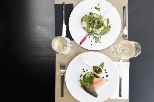 Meals for two at the restaurant served at the table, with a warm goat salad and a filet of salmon and glasses of white wine