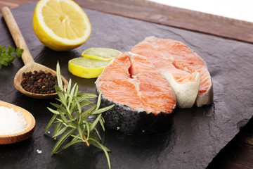 Fresh raw salmon fish steaks with fresh herbs on stone background