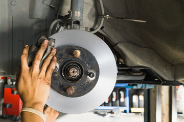 close up of hand replacing a new disc brakes of lifted automobile at auto repair garage shop station