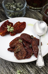 tomato fruits, dried tomatoes, san dried tomatoes, capers and herbs on a wooden table. top view