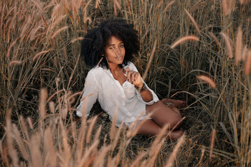 attractive young african american woman sitting on field at sunset
