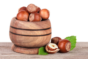 Hazelnuts with leaves in a wooden bowl on a wooden table with a white background