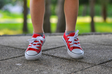 Fototapeta na wymiar Legs of a boy and his mom red shoes on the street asphalt. Big and small feets in red sneakers 