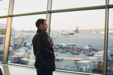 Travel concept with young man in airport interior with city view and a plane flying by.