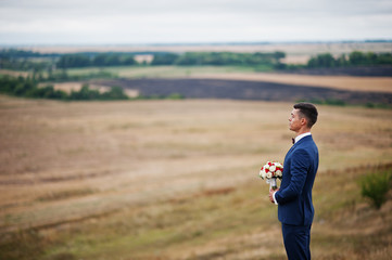 Handsome groom in the middle of the meadow surrounded by tall grass, bushes and rocks.