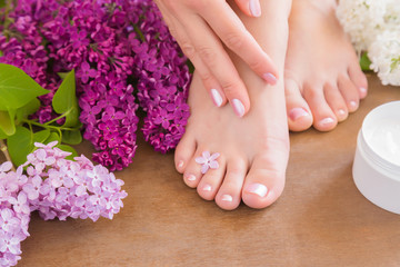 Obraz na płótnie Canvas Young woman's hand applying a foot moisturizing cream. Smooth skin. Spring and summer atmosphere with fresh, fragrant lilac flowers.