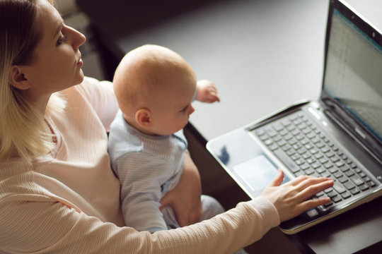 Young mother in home office with computer and her baby. Freelancer or blogger, work and child care.