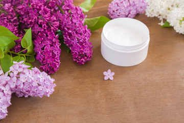 Fototapeta na wymiar Body cream with fresh, fragrant lilac flowers on the wooden background.