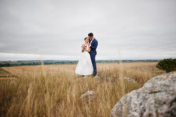 Fantastic wedding couple walking in the tall grass with the pine trees and rocks in the background holding hands.