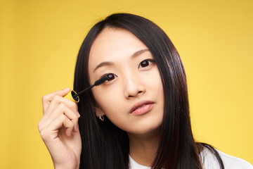 Woman is painting eyelashes, woman with mascara on yellow background