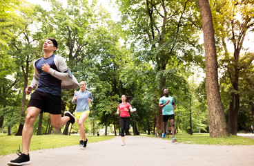 Group of young athletes running in green sunny park.