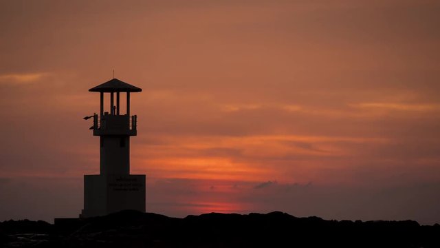 Time lapse silhouette light house with the Sun falls on the sea at sunset time.