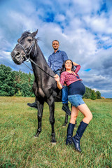 Awaiting the child, walking on the meadow. Young couple - she is a handsome brunette with long hair, pregnant; he is tall and brave, astride a black horse.