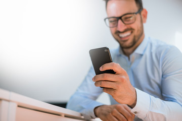 Happy bearded businessman using phone while sitting in office.