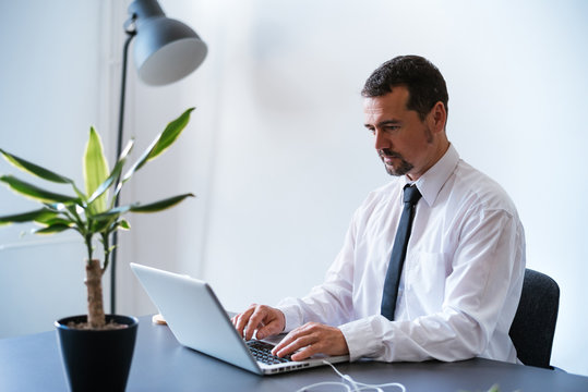 Mature Hispanic Man Using Laptop On Desk In Office