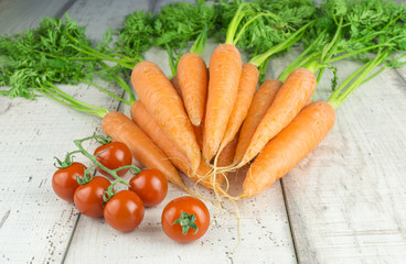 Ein Bund Möhren und einige Strauchtomaten auf Holzhintergrund