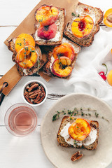 Summer snack: sandwiches with grilled peaches, cream cheese, thyme and pecan with a glass of chilled rose wine on distressed white wooden background