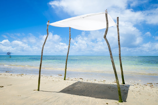 Rustic sun shade made from a sheet strung from sticks stands on an empty beach in Bahia, Brazil