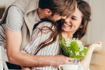 Young casual couple embracing with bouquet of flowers at home