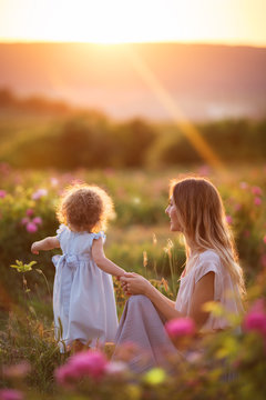 Beautiful child girl with young happy mother are wearing casual clothes walking in roses garden over sunset lights, summer time