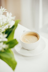 close up of cup of coffee with bouquet of flowers on white tabletop