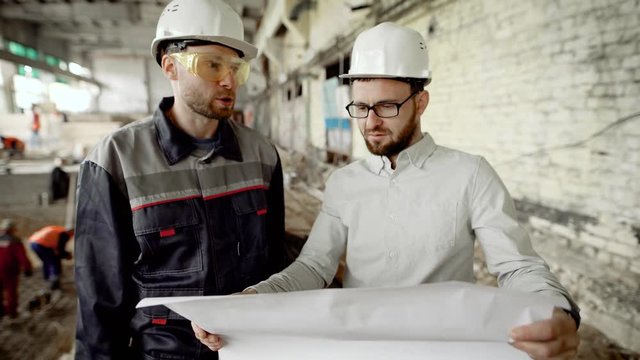Architect and worker at the construction site of the plant. The chief architect looks through the drawing and decides on further work.