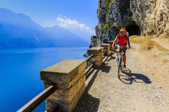 Mountain biking woman over Lake Garda on path Sentiero della Ponale, Riva del Garda, Italy