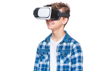Happy teen boy wearing virtual reality goggles watching movies or playing video games, isolated on white. Cheerful teenager looking in VR glasses. Funny child experiencing 3D gadget technology.