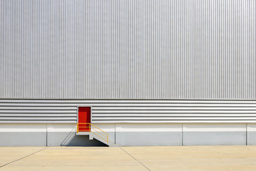 The red exit door at the sheet metal wall of factory building.