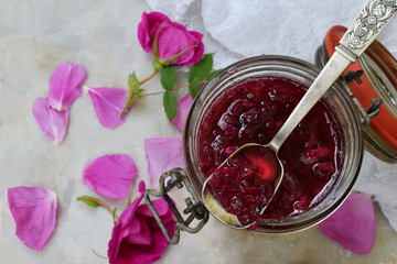 Glass jar and little spoon with tea rose petal jam on light marble background. Copy space for text.