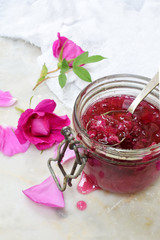 Glass jar and little spoon with tea rose petal jam on light marble background. Copy space for text.
