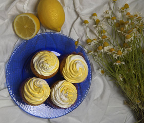 Fototapeta na wymiar delicious freshly baked homemade lemon muffins cupcakes with butter cream with bouquet of chamomile flowers , copy space