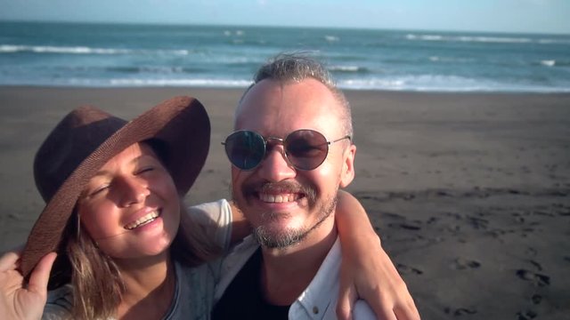 Romantic couple in the sunlight taking selfie portrait video picture on beach with camera or smart phone. Young couple on holidays enjoying new adventures, relaxation and travel.