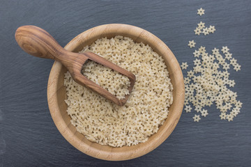 Red rice and olive wood scoop on black background of slate or stone. 