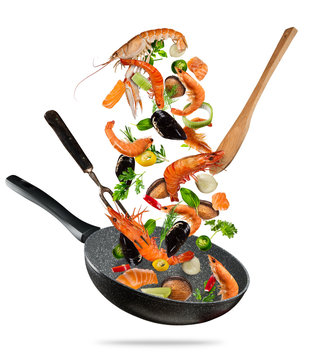 Fresh sea food and vegetables flying into a pan on white background