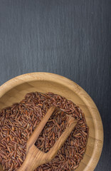 Red rice and olive wood scoop on black background of slate or stone. Vertical image