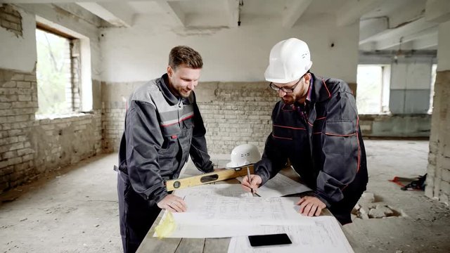 Building object. Master and worker at the table with a drawing. The foreman looks through and corrects the main plan of the construction project.