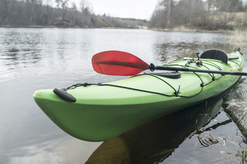 Green kayak is moored on the shore of the lake, against the background of the forest and the cloudy...