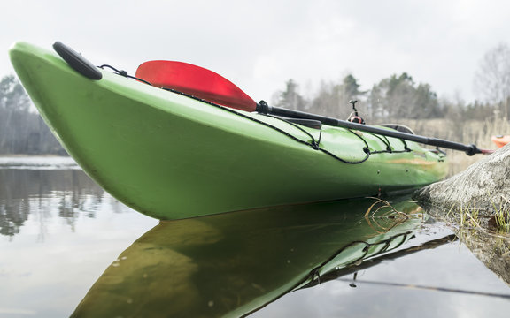 Green kayak is moored on the shore of the lake, against the background of the forest and the cloudy sky.