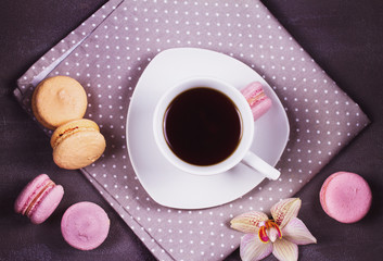 Coffee, orchids and cake macaron or macaroon on gray background from above. Flower, drink and coockie still life. Flat lay, top view. Soft pink toning