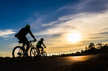 Obraz premium Silhouette of cyclists riding bikes on road at sunset.