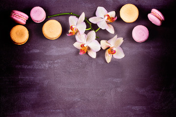 Obraz na płótnie Canvas Orchids and cake macaron or macaroon on gray background from above. Flat lay, top view. Flower and cookie still life. Soft pink toning, copy space
