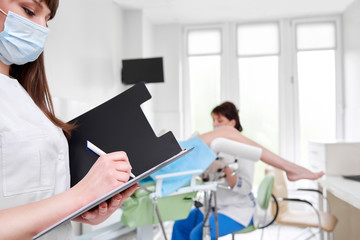 Obraz premium Cropped shot of a nurse writing on her clipboard professional gynecologist examining her patient on the gynecological chair on the background copyspace medicine gynecology health concept.