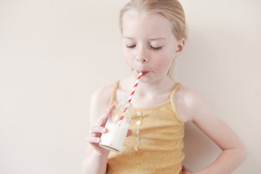 Young girl drinking glass of milk through straw