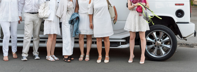 People dressed in white posing next to limousine. Body parts, white party