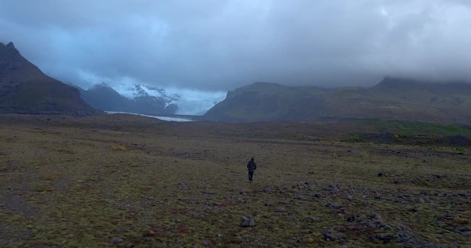 ICELAND – SEPTEMBER 2016 : Aerial shot of man running towards glacier on a cloudy day