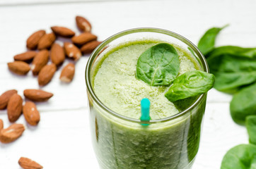 Spinach smoothie on a wooden white background. Glass of smoothie with two leaves of spinach. Nuts. Healthy food. Breakfast.