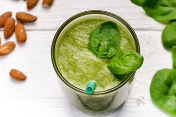 Spinach smoothie on a wooden white background. Glass of smoothie with two leaves of spinach. Nuts. Healthy food. Breakfast.